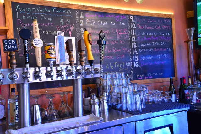 Some of the 16 taps and beer menu board behind them.